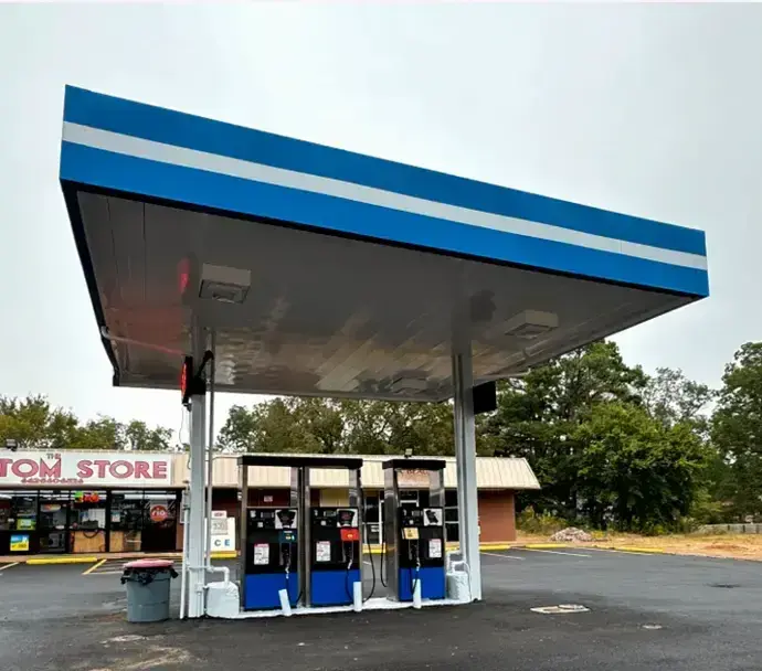 Gas station with blue-striped canopy and fuel pumps in front of a convenience store / HSO Technology /